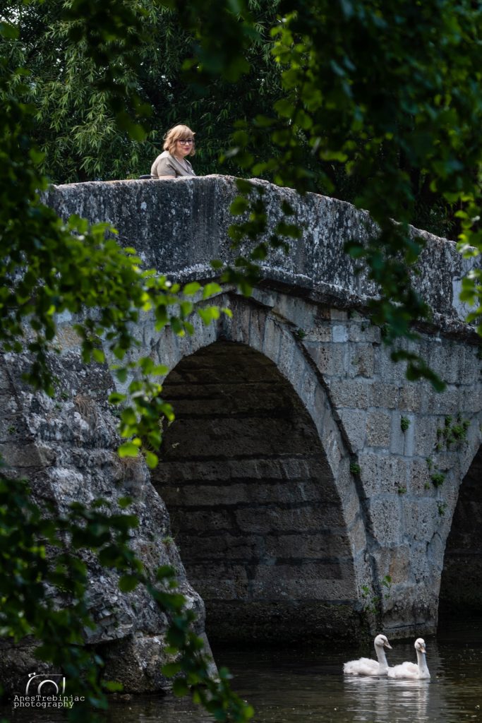 Stari kameni most obrastao zelenilom, osoba stoji na mostu